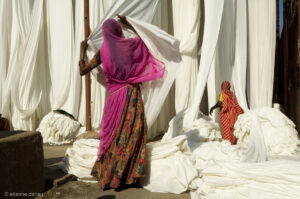 femme déplacant des tissus après les phases de teinture et de séchage, dans une usine indienne de sari.